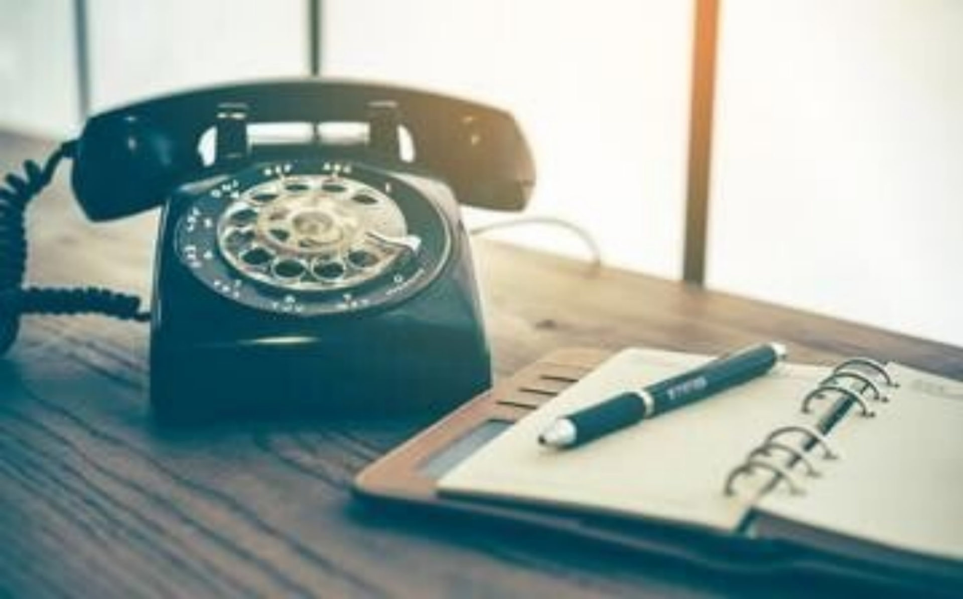 Auf einem Holztisch liegen ein Vintage-Telefon, ein Notizbuch und ein Stift, im Kontext mit Jenseitskontakte Jana Lorenz.