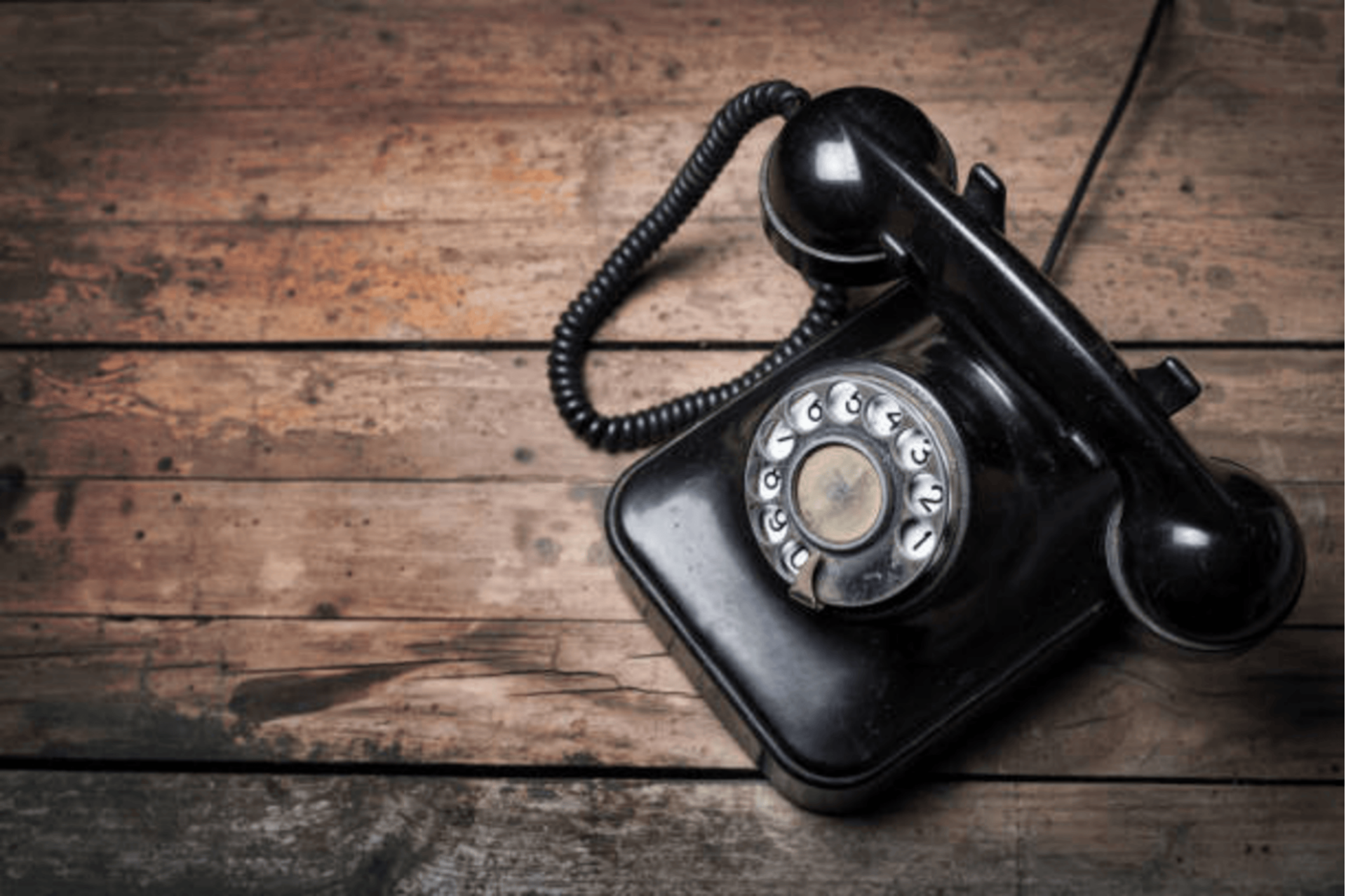 Ein schwarzes, klassisches Telefon mit Wählscheibe und Hörer liegt auf einem rustikalen Untergrund aus dunklen, horizontal verlaufenden Holzplanken, im Kontext mit Jenseitskontakte Jana Lorenz.