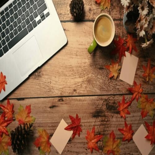 Ein Laptop und bunte Herbstblätter sind auf einem Holztisch arrangiert, was eine einladende Arbeitsumgebung schafft, im Kontext mit Jenseitskontakte Jana Lorenz.