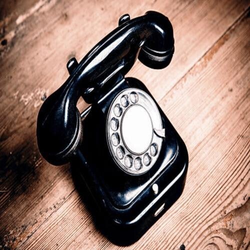 Ein klassisches, glänzend schwarzes Telefon mit Wählscheibe steht auf einem rustikalen Untergrund aus hellbraunen, strukturierten Holzdielen, im Kontext mit Jenseitskontakte Jana Lorenz.