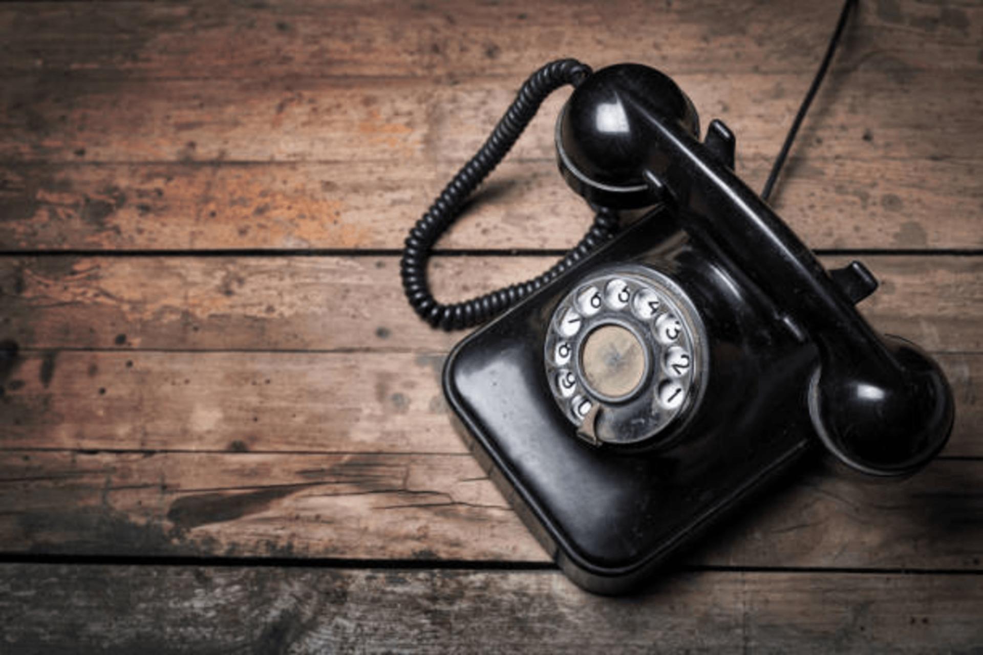 Ein schwarzes, klassisches Telefon mit Wählscheibe und Hörer liegt auf einem rustikalen Untergrund aus dunklen, horizontal verlaufenden Holzplanken, im Kontext mit Jenseitskontakte Jana Lorenz.