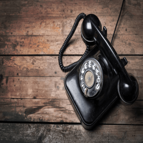 Ein schwarzes, klassisches Telefon mit Wählscheibe und Hörer liegt auf einem rustikalen Untergrund aus dunklen, horizontal verlaufenden Holzplanken, im Kontext mit Jenseitskontakte Jana Lorenz.
