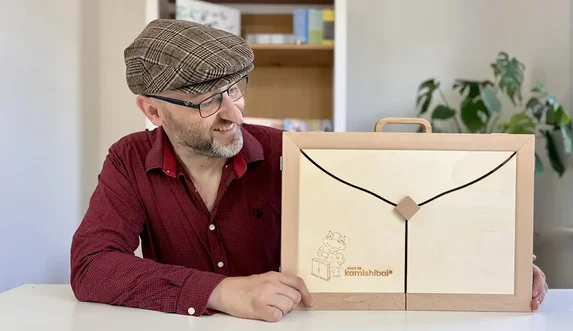 Man met pet toont houten kamishibai-theater met logo Start to Kamishibai