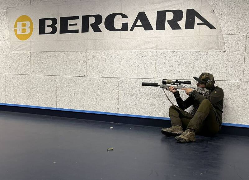 Ein Jäger sitzt auf dem Boden und zielt mit seiner Bergara-Kipplaufbüchse in der linken Hand.