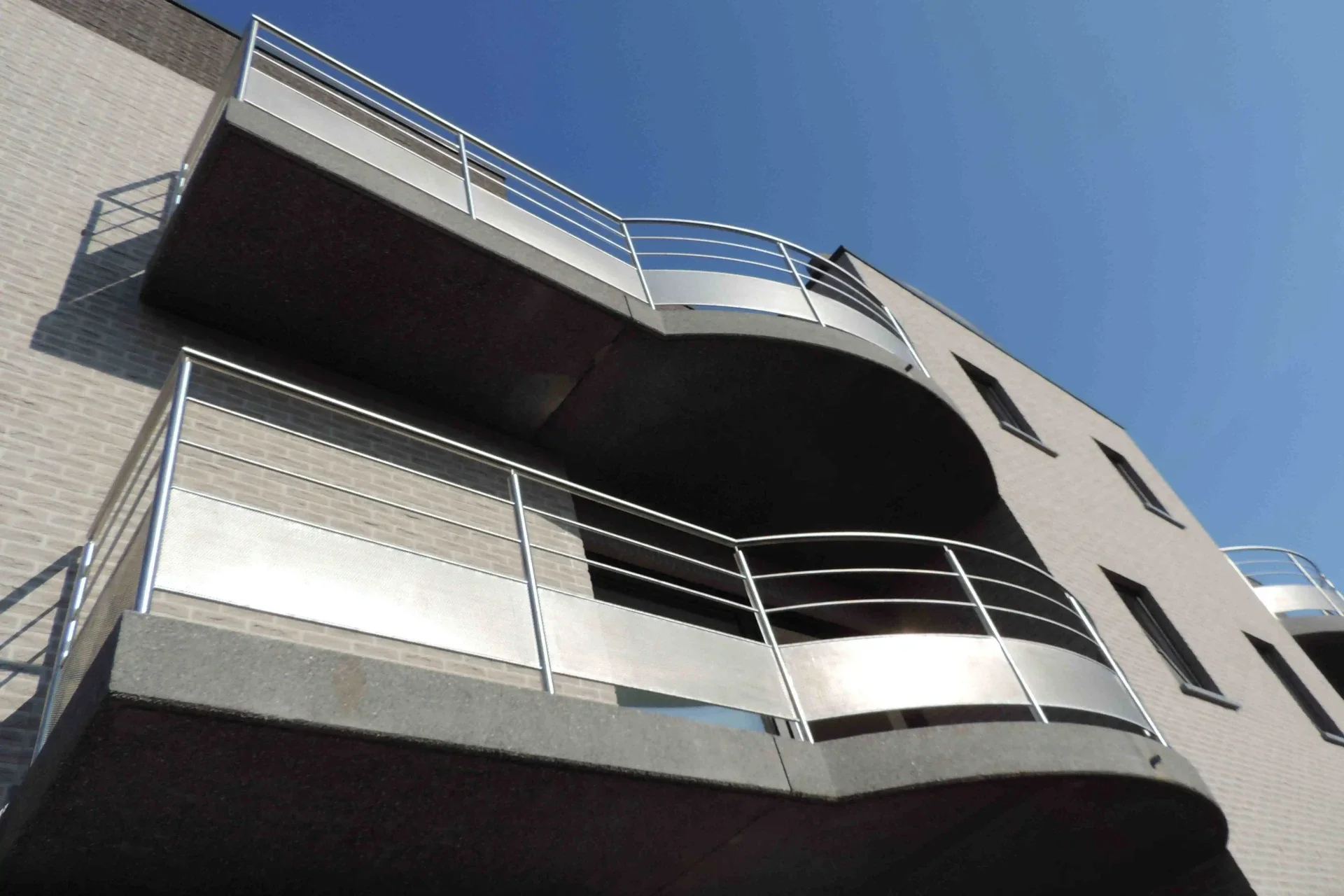 Gebogen inox balustrade met doorvalbeveiliging in rond geperforeerde inox plaat.