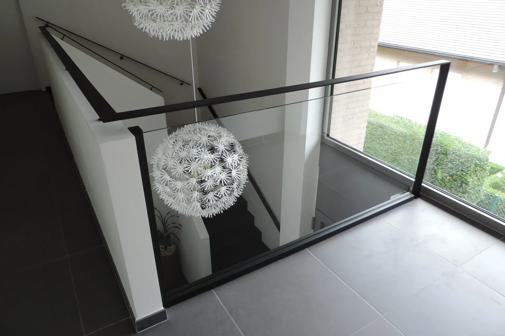 Zwarte metalen trapleuning met  glasbalustrade aan vide.