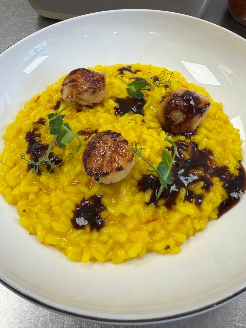 Saffron risotto topped with seared scallops and veal jus, a sophisticated fusion of land and sea.