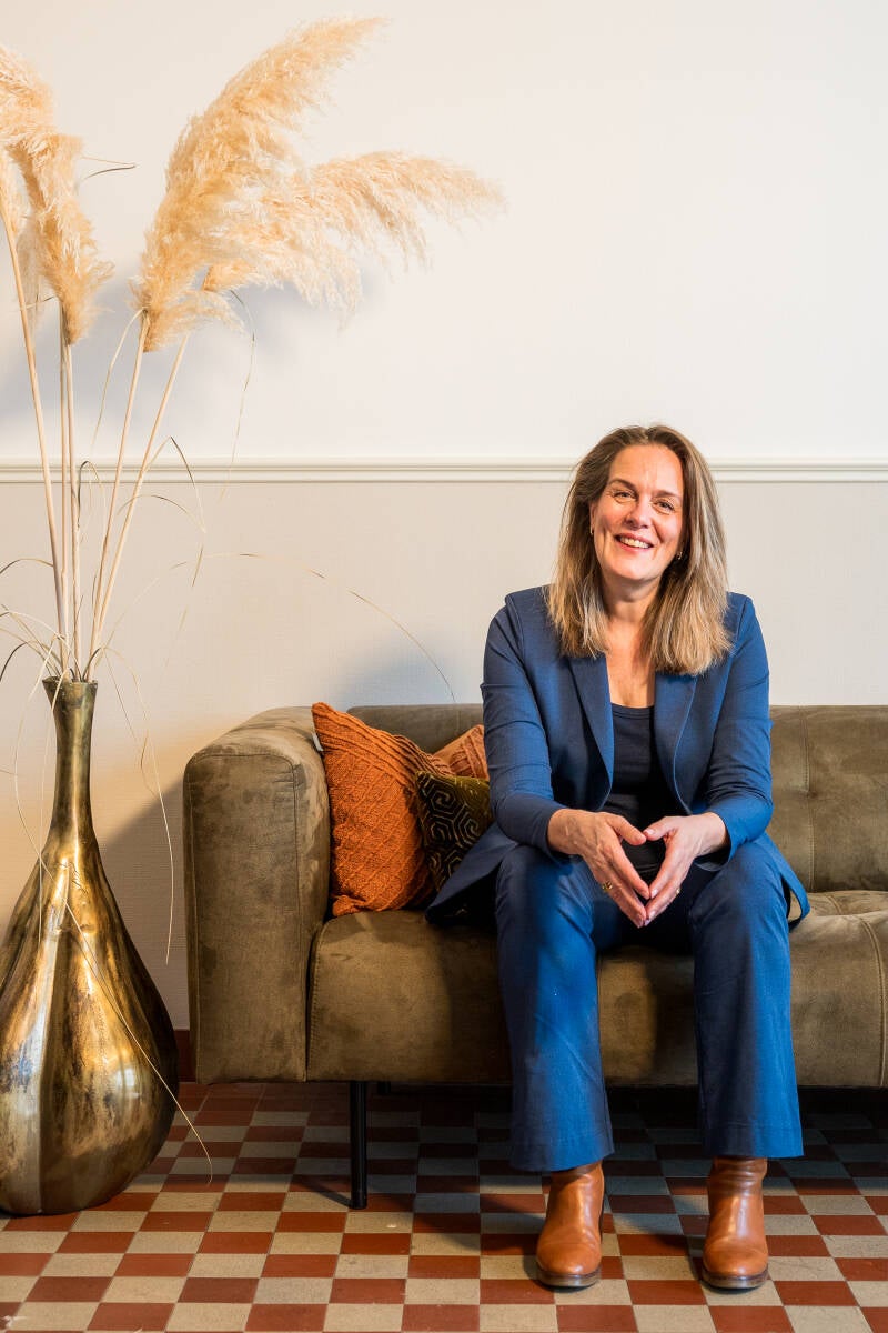Een vrolijke en toegankelijke Judy Kamsteeg, loopbaancoach, zittend op een bank tijdens een gesprek over wie zij is.