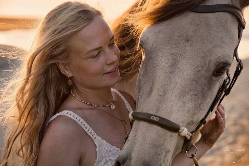 Junge Frau schmust mit ihrem Pferd am Strand im Gegenlicht.