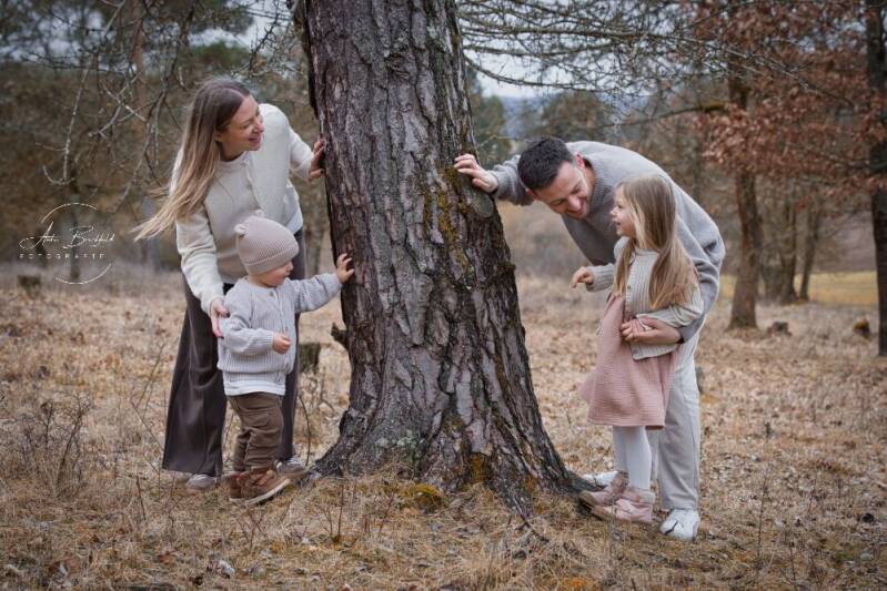 Familie mit zwei kleineren Kindern schauen um einen Baum herum.