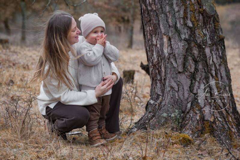 Mutter kniet neben kleinem Sohn neben einem Baum.