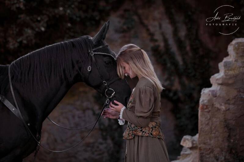 Junge Frau und ihr Pferd Kopf an Kopf in einer Burg.