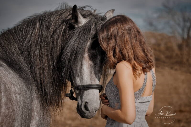 Junge Frau im Glitzerkleid schmust mit Pferd.