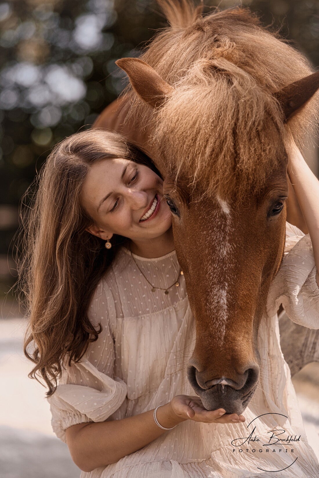 Junge Frau sitzt vor ihrem Pferd, Das Pferd legt seinen Kopf über ihre Schulter.