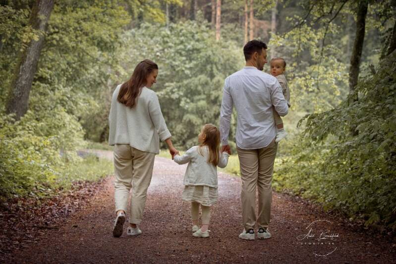 Familie mit zwei Kindern läuft einen Waldweg entlang.