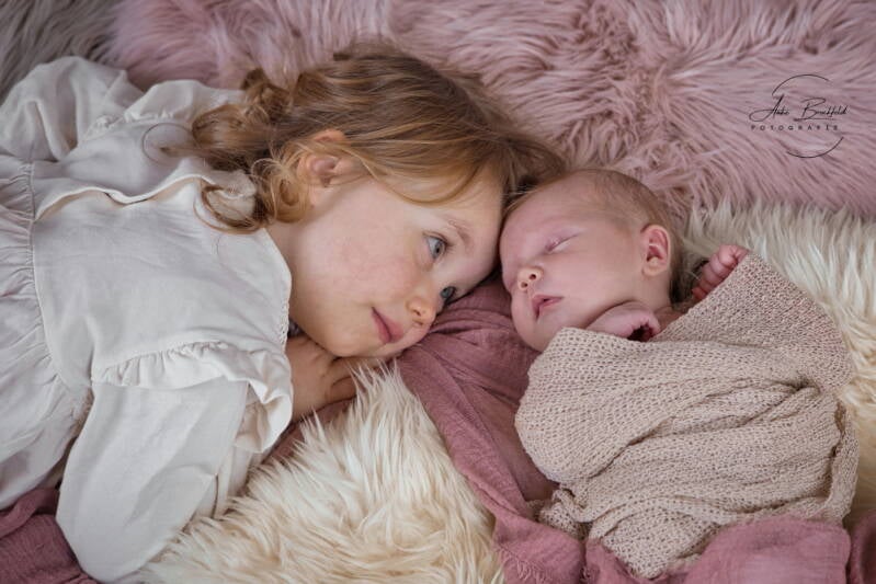 Schwester kuschelt im Liegen mit Neugeborenem.