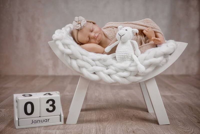 Neugeborenes schläft auf weißem Schemel.