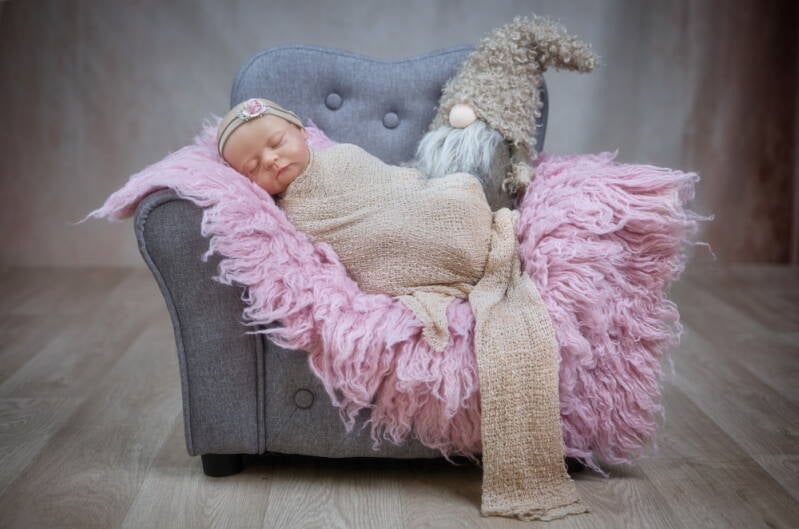 Neugeborenes schläft eingewickelt auf Mini-Sessel.