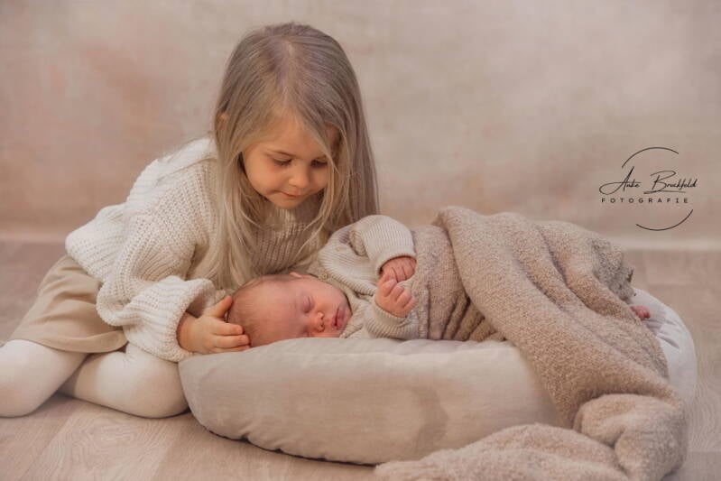 Große Schwester streichelt vorsichtig das Neugeborene.