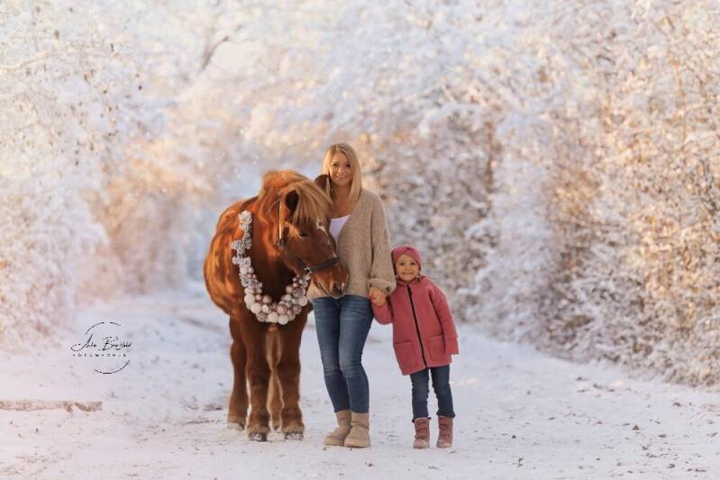Mutter und Tochter stehen in Schneelandschaft neben einem Pferd.