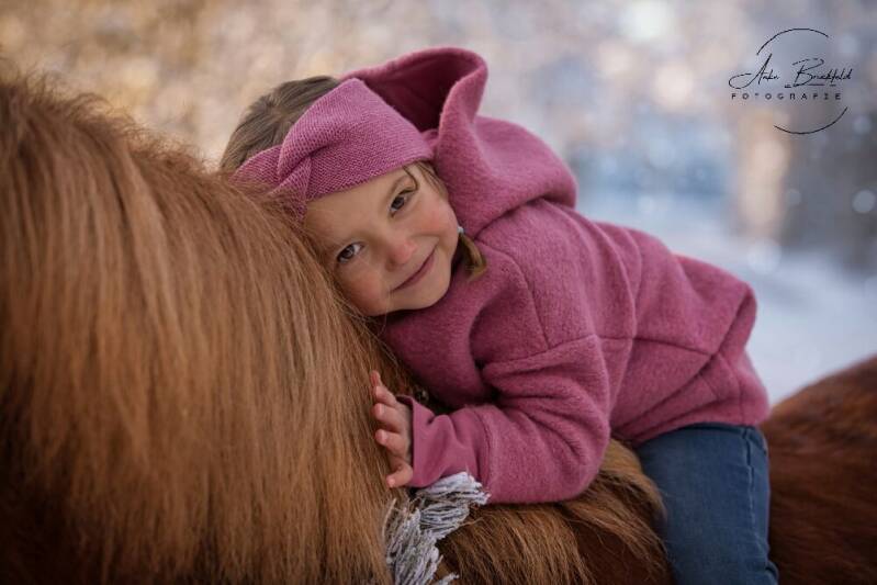 Kleines Mädchen liegt auf dem Hals eines Pferdes.