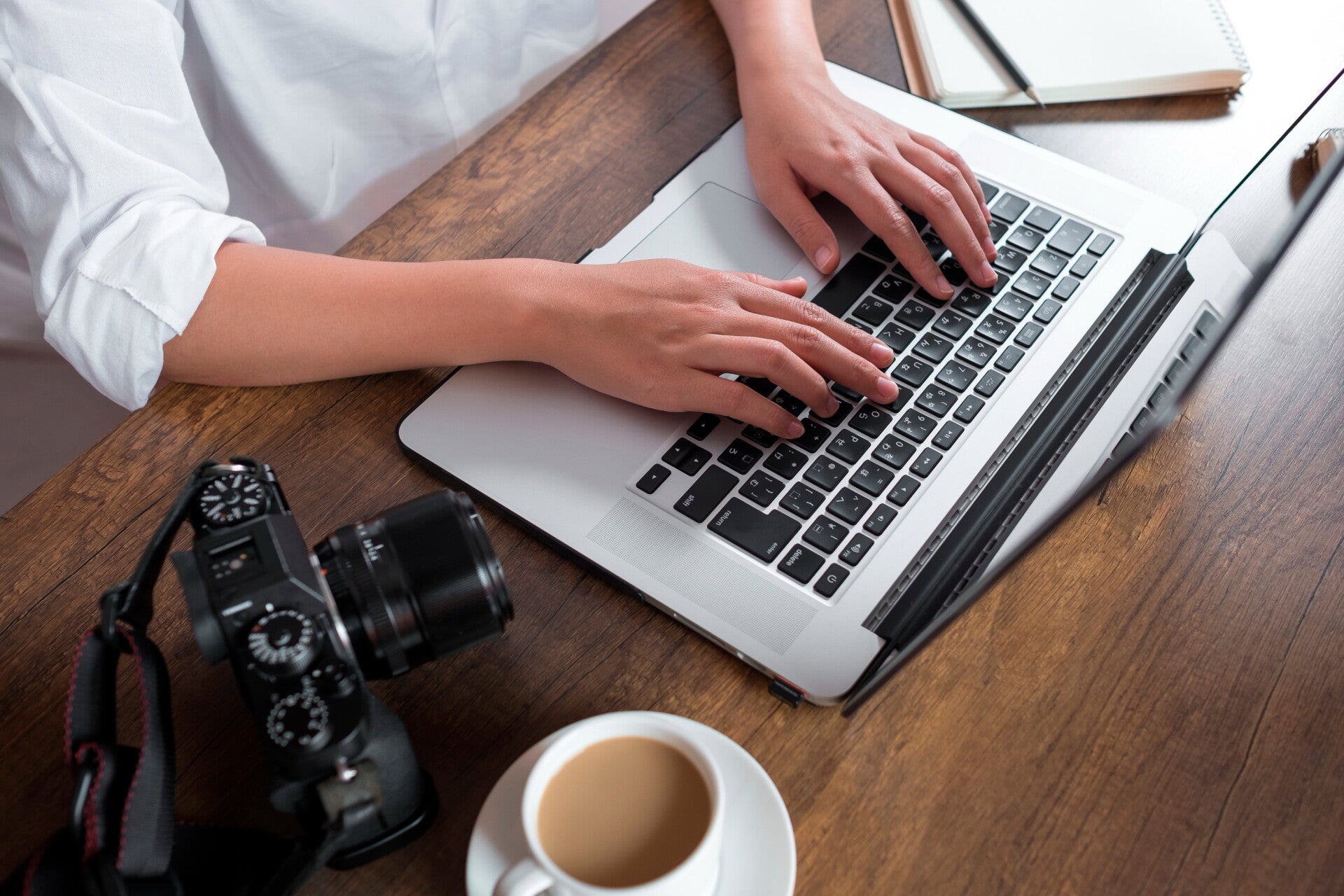 Laptop, Kaffeetasse und Kamera auf Holztisch.