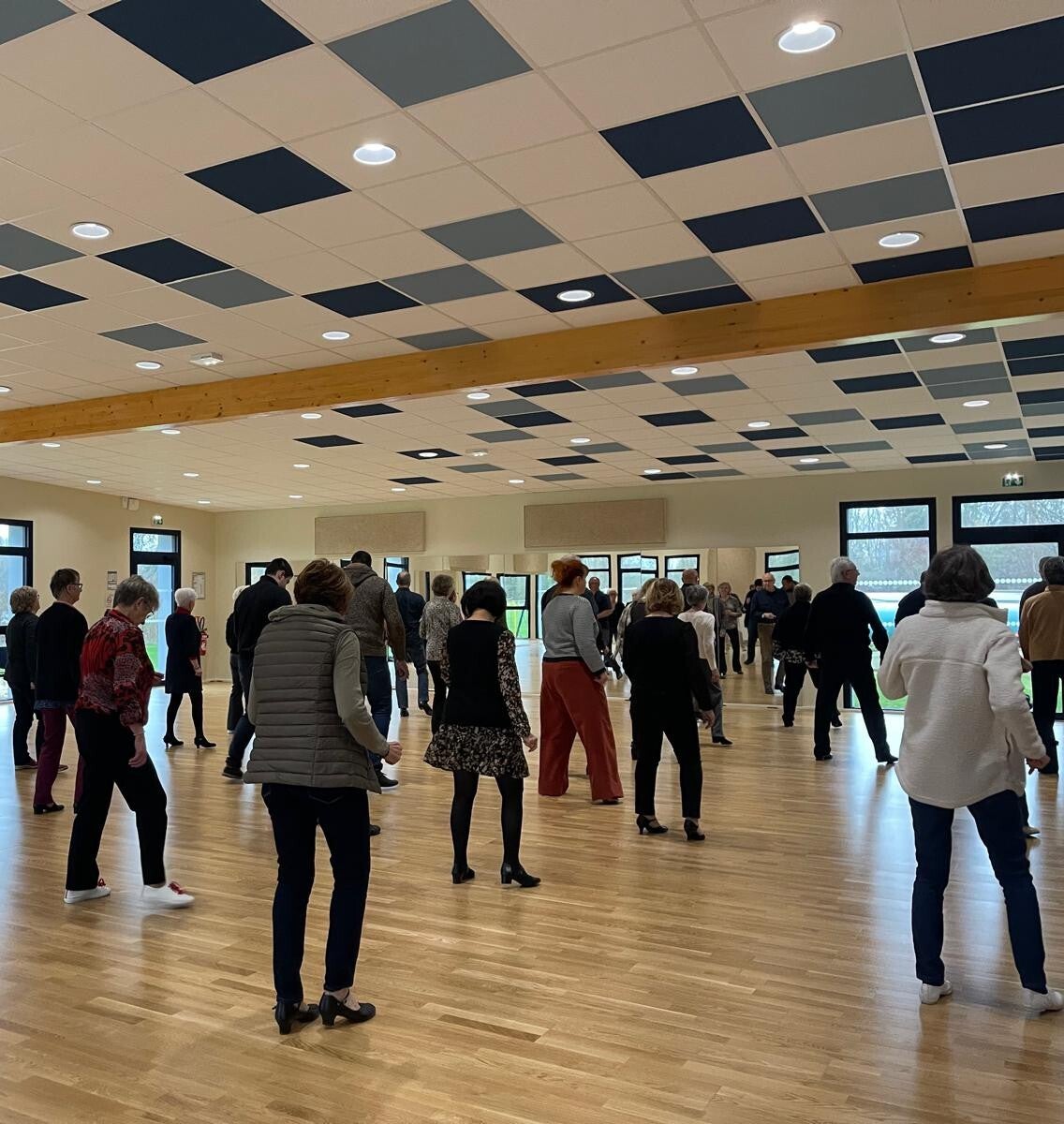 Groupe d'adhérents dansant en ligne dans la grande salle de L'Académie, alignés sur plusieurs rangs