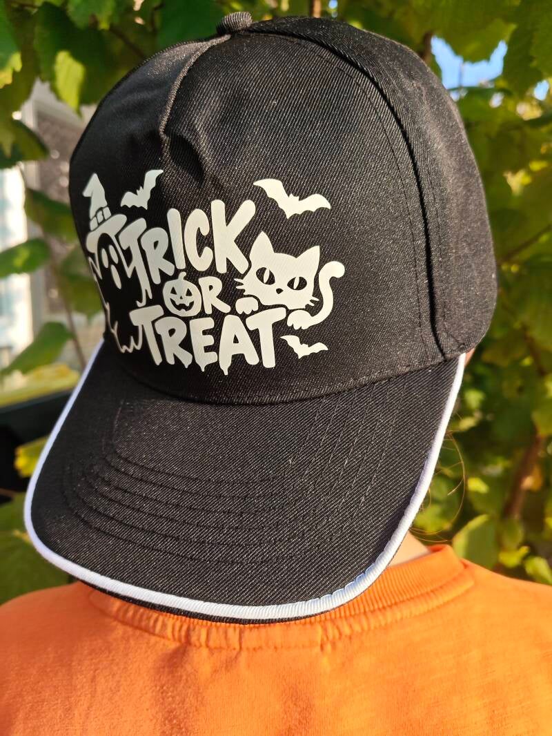 Trick-or-treat cap zwart met witte bies, bij daglicht. Deze licht op in de avond als het donker wordt.