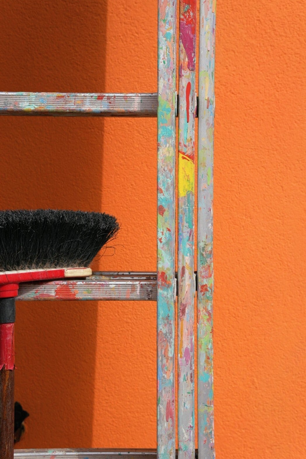 Photo artistique d'une échelle et d'un balai en appui contre un mur orange, maison de Burano (Italie)