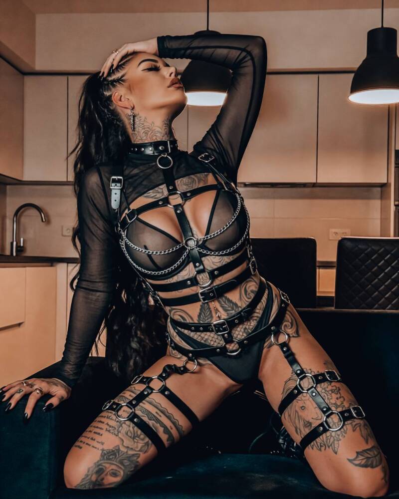 Tattoo Model Phina Offizial in schwarzem Harness Outfit mit Tattoos – sinnliches Pose in moderner Küche