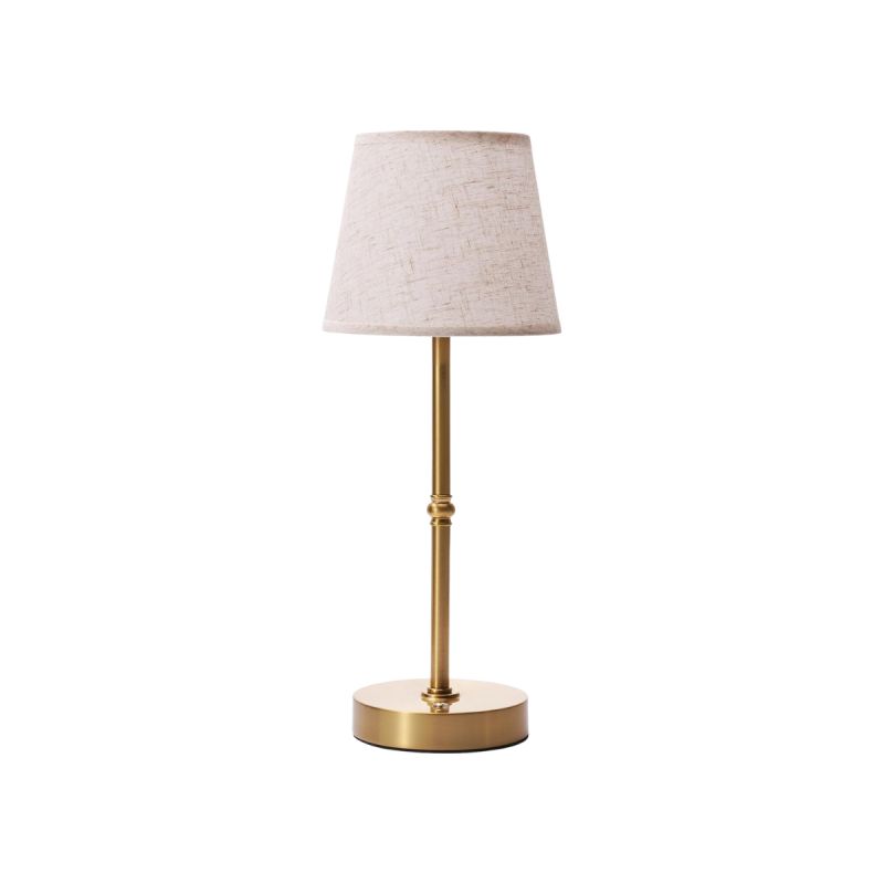 A small cordless table lamp with a fabric shade casting warm light in a cozy, minimalist room.