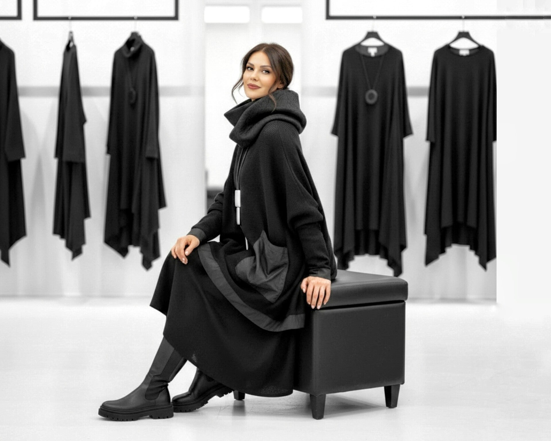 Eine extravagant gekleidete Frau sitzt lächelnd auf einem Hocker in einer Modeboutique 