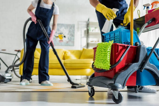 Professional cleaners vacuuming and organizing a modern living room, delivering spotless results with a well‑equipped cleaning setup.