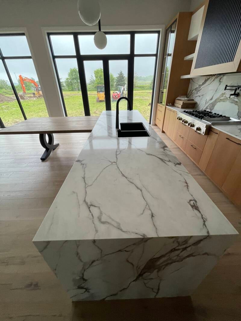 Bright modern kitchen with a spotless marble island, clean wood cabinetry, and streak‑free windows showcasing professional cleaning quality.