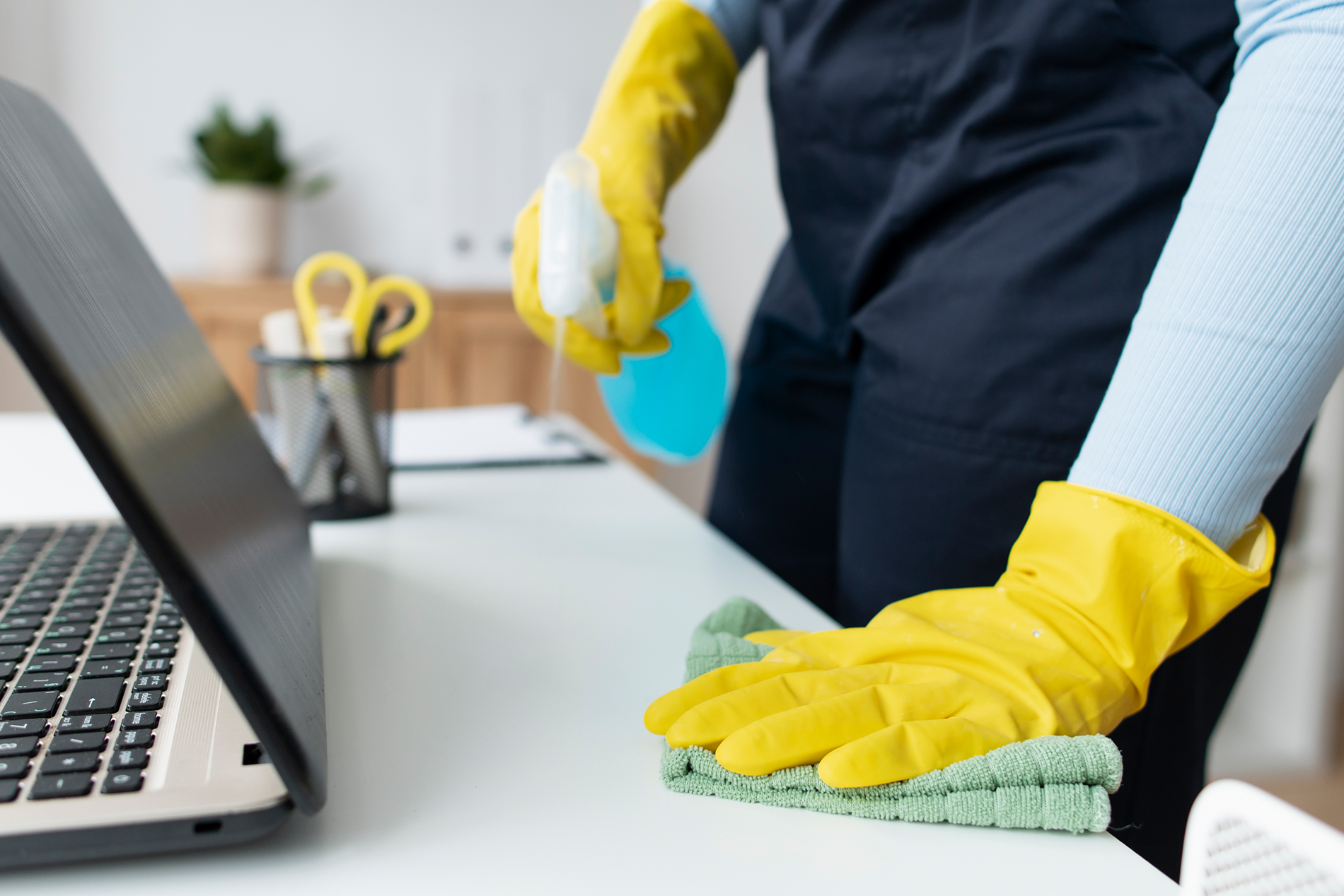 Desk cleaning in a modern workspace with spray and microfiber cloth, delivering hygienic, professional surface care.