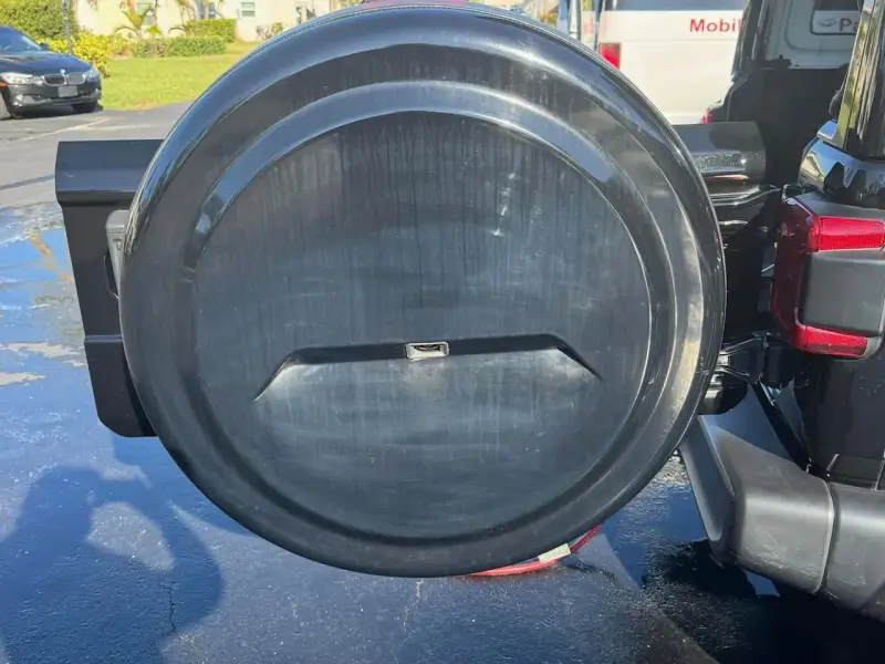 Scratched and faded black spare tire cover on the back of a Mercedes, showing signs of UV damage and oxidation.
