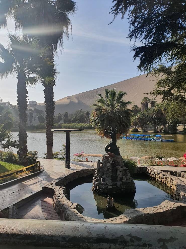De oase van Huacachina bij Ica in Peru, met een lagune, palmbomen, bebouwing en hoge zandduinen midden in de woestijn.