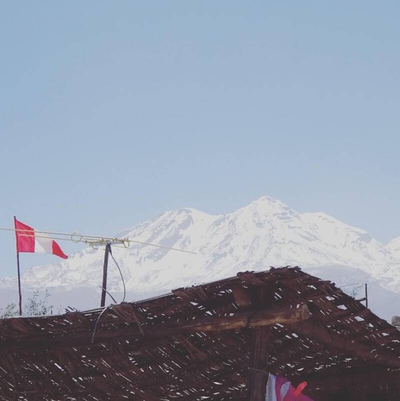Peruaanse vlag boven een eenvoudige houten constructie met een grote besneeuwde berg in de Andes op de achtergrond.