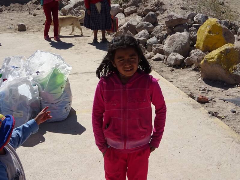 Meisje in roze kleding op een stoffige weg in Peru, naast zakken met ingezamelde kleding en speelgoed.