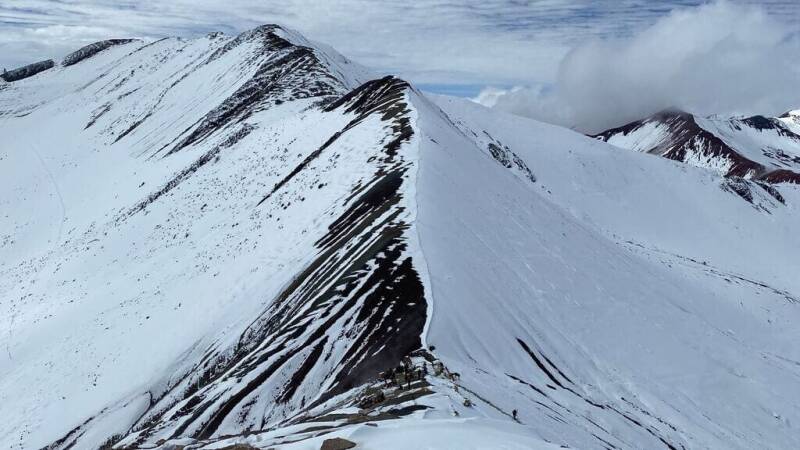 Rainbow Mountain (Vinicunca) in Peru met besneeuwde bergkam en uitzicht over de Andes.