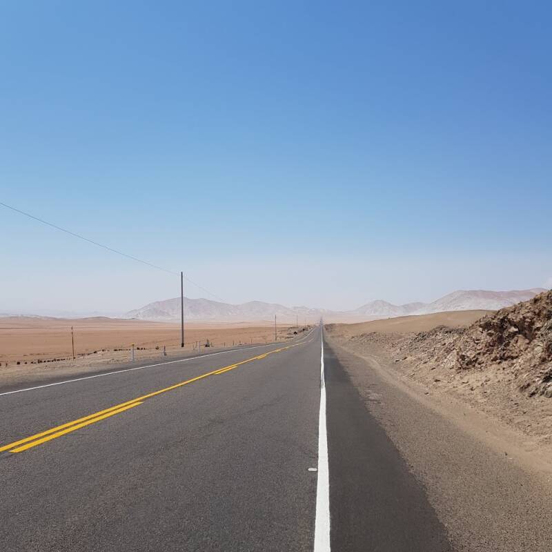 De Panamericana Sur tussen Moquegua en Tacna in Peru, een verlaten asfaltweg door een uitgestrekt woestijnlandschap met bergen aan de horizon.