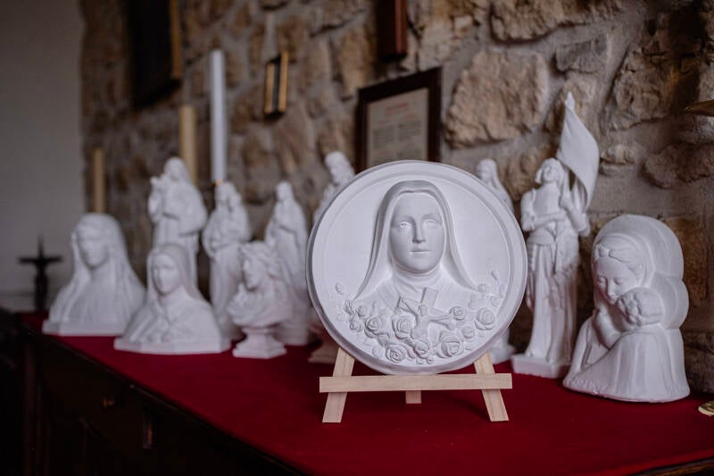 Grande médaille de Sainte Thérèse de L'enfant Jésus au milieu d'autres bas reliefs en platre produits en Dordogne de manière artisanale.