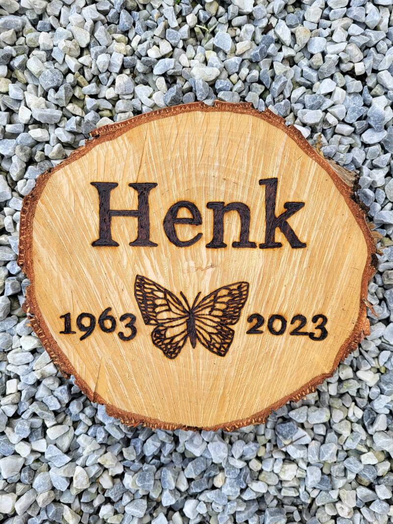 Boomschijf voor op de Natuurbegraafplaats van Henk houtgebrand met vlinder, geboortejaar en overlijdensjaar.