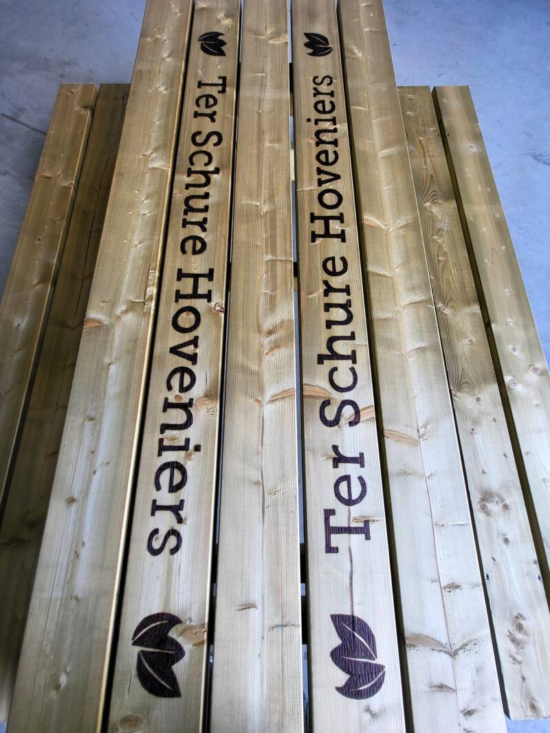 Picknick tafel met twee keer het logo Ter Schure Hoveniers erop houtgebrand van dichtbij