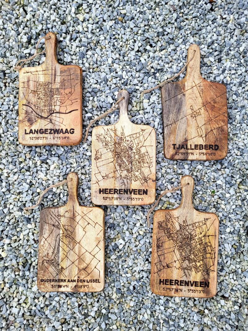 Vijf mangohouten borrelplanken met plattegronden van woonplaatsen erop. 