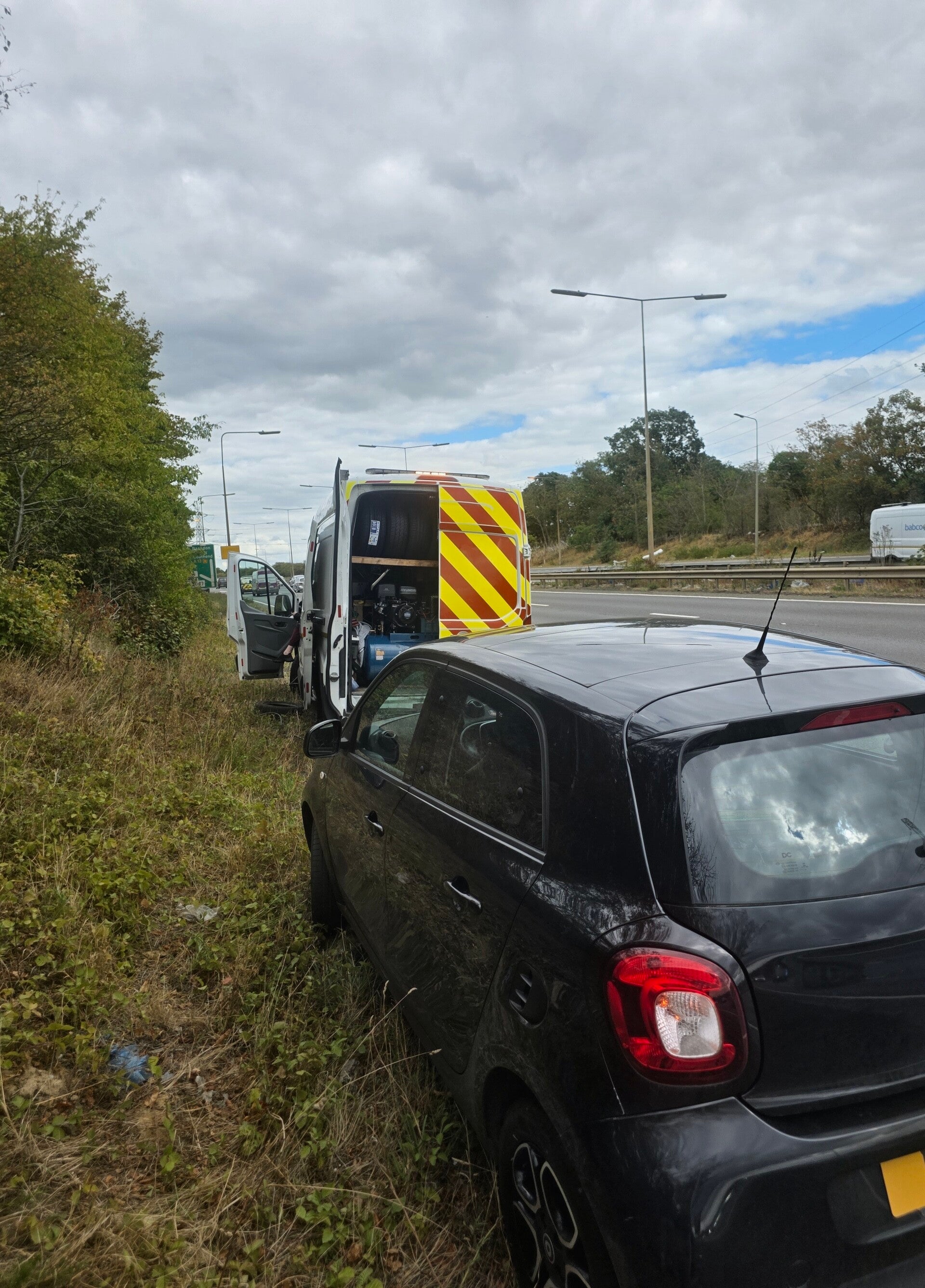 Emergency mobile tyre fitting at the roadside, with a stranded car and tyre fitting van attending the breakdown.