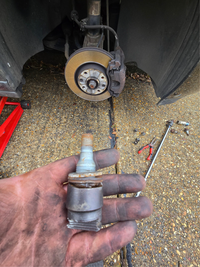 Removed locking wheel bolt held in front of a vehicle with the wheel removed.