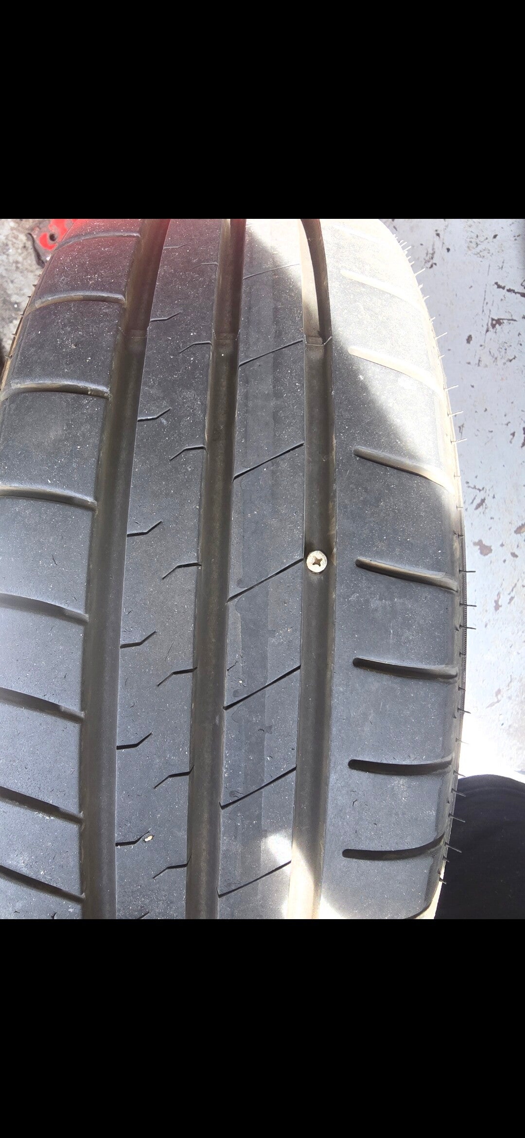 Close-up of a screw embedded in a car tyre tread causing a puncture.