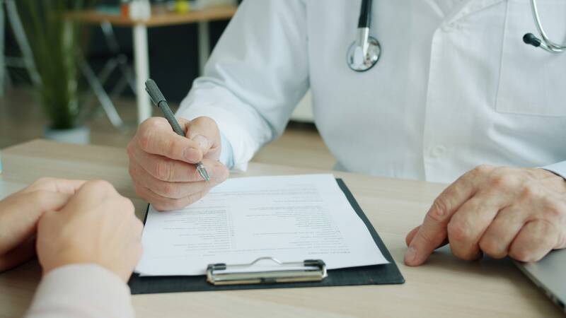 Un doctor llenando una forma en suescritorio, puedes ver las manos de el paciente