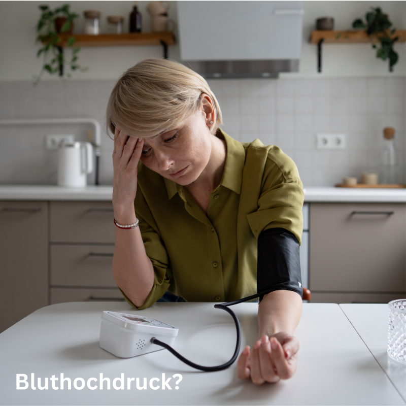 Eine Frau misst zu Hause ihren Blutdruck am Tisch und wirkt besorgt, Thema Bluthochdruck natürlich senken und Zellregeneration mit Pura Vida Glow.